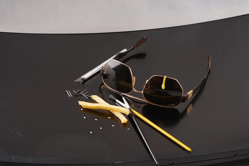 Lunettes et outils – entre food et précision Lunettes de soleil avec outils de précision, frites et goutte de sauce sur fond noir