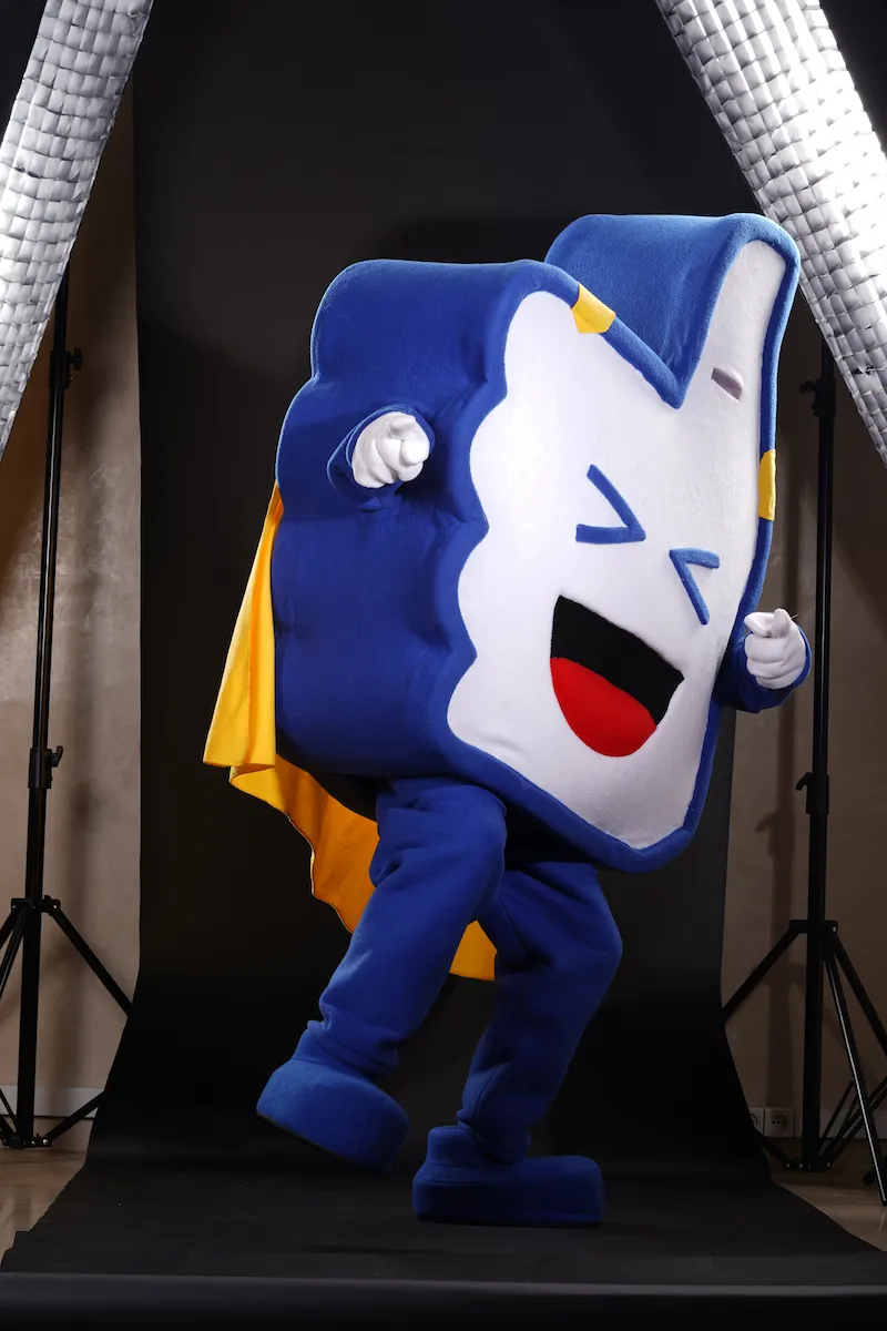 Mascotte Superlikeman d’Allogood, en costume bleu et jaune, en pleine pose dynamique pour les réseaux sociaux
