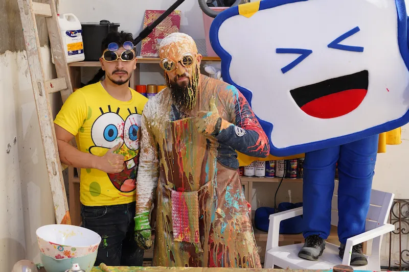 Superfoodman couvert de peinture aux côtés d’un artiste en tee-shirt Bob l’éponge, dans le studio Allogood avec Superlikeman en arrière-plan